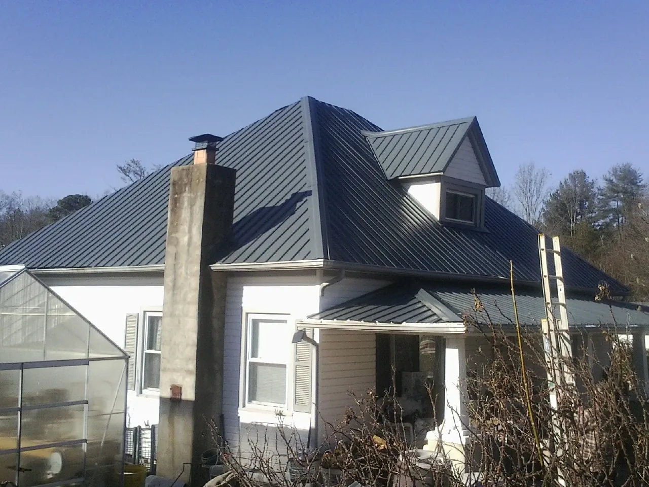 Dark blue standing seam metal roof on a white farmhouse with dormer — Slate & Tile Roof Repair by Roofing Brothers in Hicksville
