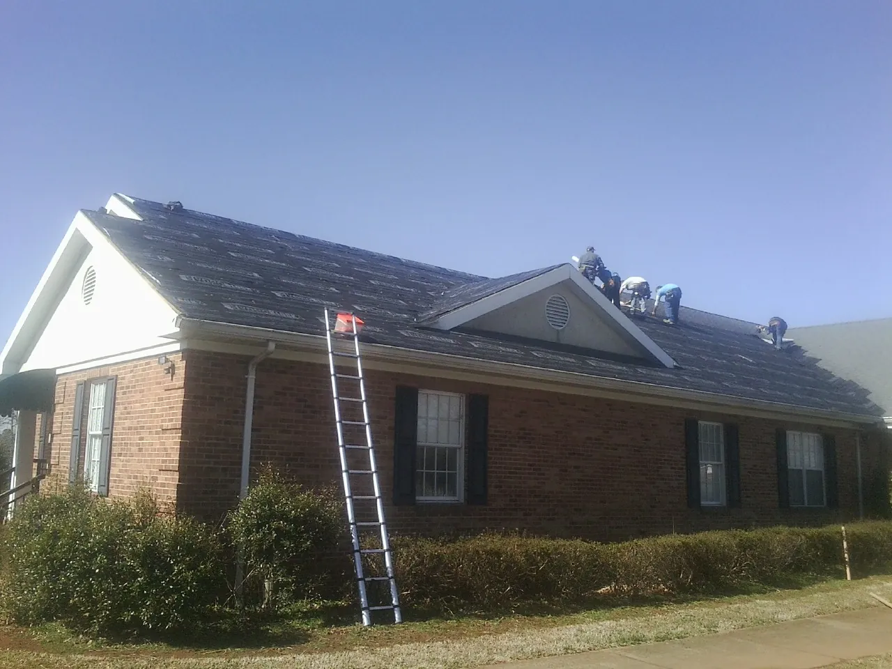 Crew tearing shingles off a brick ranch roof with a ladder set — Emergency Roof Repair work by our crew in Hicksville
