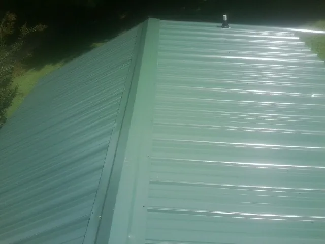 New green metal panels meeting at the ridge of a roof — Flat Roof Repair work by our crew in Hicksville