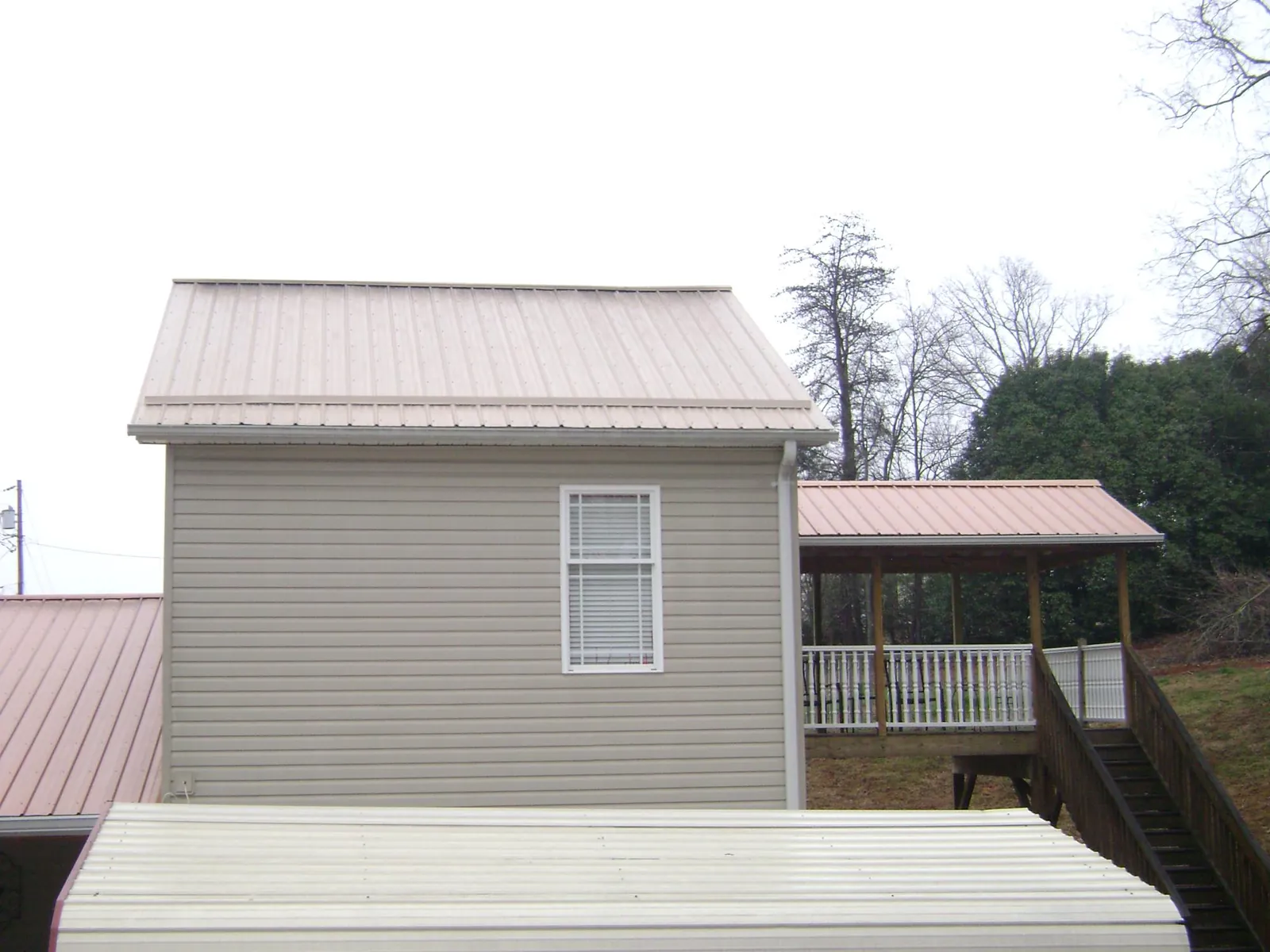 Tan metal roofs on a two story addition and attached porch, from a Roof Replacement job in Hicksville